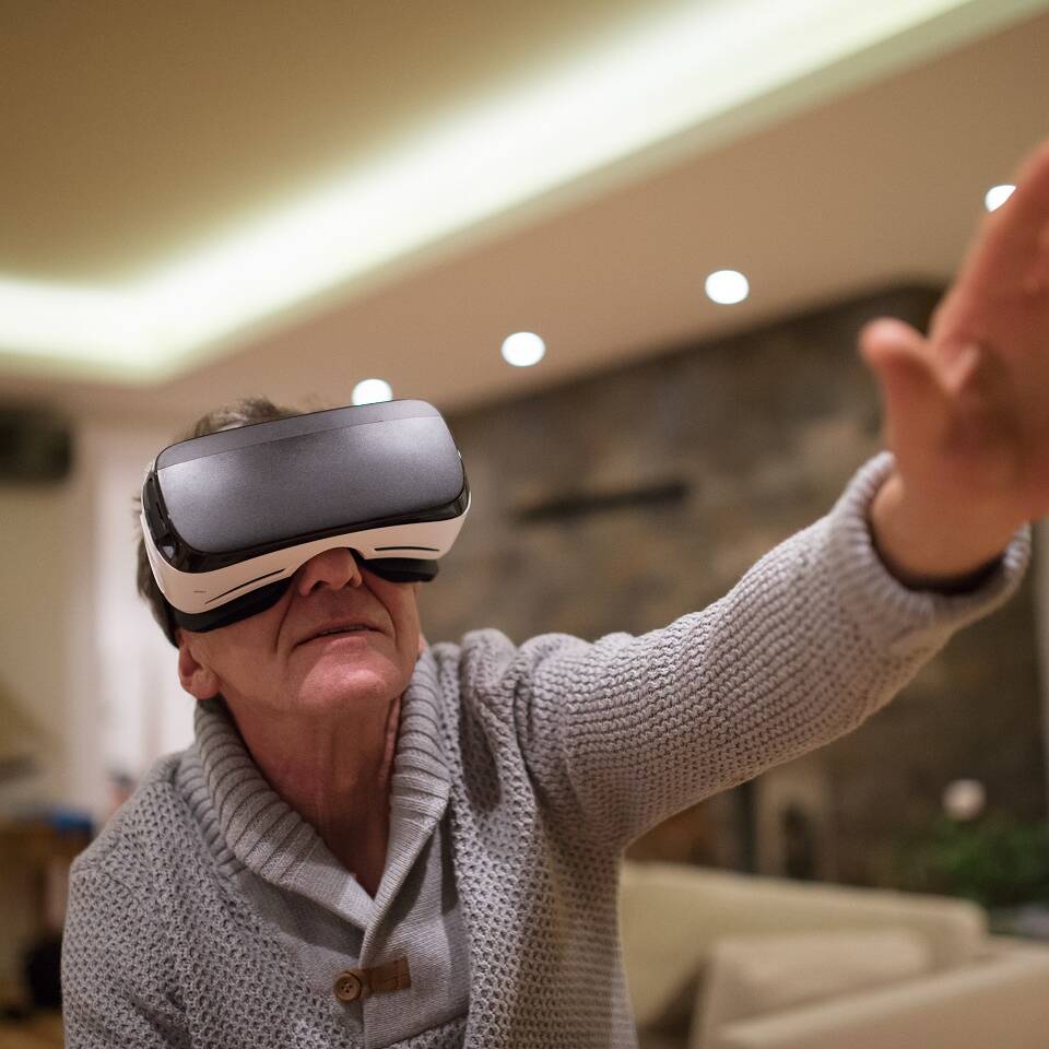 Senior man wearing virtual reality goggles at home